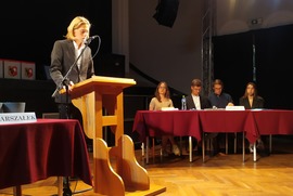 Zdjęcie przedstawia chłopaka stojącego za mównicą. W tle widać drużynę biorącą udział w debacie. (photo)