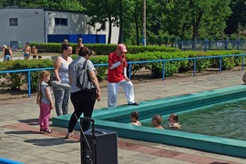 Zdjęcie przedstawia basen, w którym pływają dzieci. Przy basenie stoi ratownik oraz trzy pozostałe osoby.  (photo)