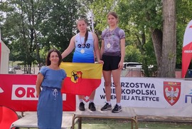 Zdjęcie przedstawia dwie dziewczynki stojące na podium oraz kobietę stojącą przed nimi. (photo)