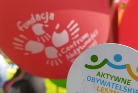 Na pierwszym planie zdjęcia widać znaczek Aktywnego Obywatelskiego Leszna, a na drugim planie znajduje się czerwony balon z logiem Fundacji Centrum Aktywności Twórczej. (photo)