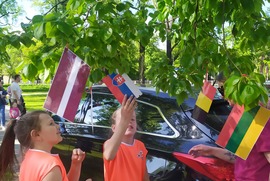 Zdjęcie przedstawia drzewo na którym rozwieszone są flagi Unii Europejskiej. Pod drzewem znajdują się dziewczynki ubrane w pomarańczowe stroje mażoretek. (photo)