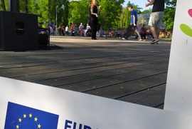 Zdjęcie przedstawia dwie osoby znajdujące się na scenie. Osoby te żąglują piłeczkami. Na pierwszym planie widać baner Europejskiego Korpusu Solidarności (photo)