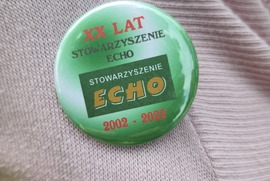 Zdjęcie przedstawia zieloną plakietkę z logo Stowarzyszenia ECHO. Napisy są zielone i czerwone (photo)