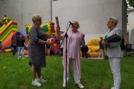 Zdjęcie przedstawia trzy kobiety. Jedna z nich przemawia do mikrofonu, kolejna trzyma kwiaty, a ostatnia grawerton. (photo)