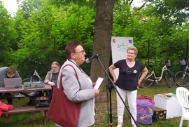 Zdjęcie przedstawia Radną Miasta Leszna przemawiającą do mikrofonu. W tle widać inną kobietę. (photo)