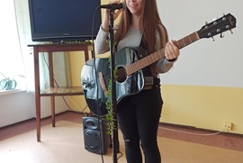 Źródło Facebook Bursa Międzyszkolna. Zdjęcie przedstawia śpiewającą i grającą na gitarze kobietę. (photo)