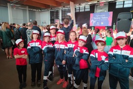 Zdjęcie przedstawia grupę tancerzy. Wszyscy ubrani są w takie same granatowo - biało -czerwone strone. Na głowach mają czapeczki z daszkiem. (photo)